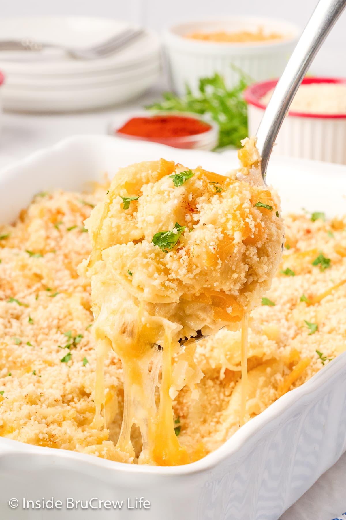 A pan of cheesy pasta with a spoon lifting the cheese up.