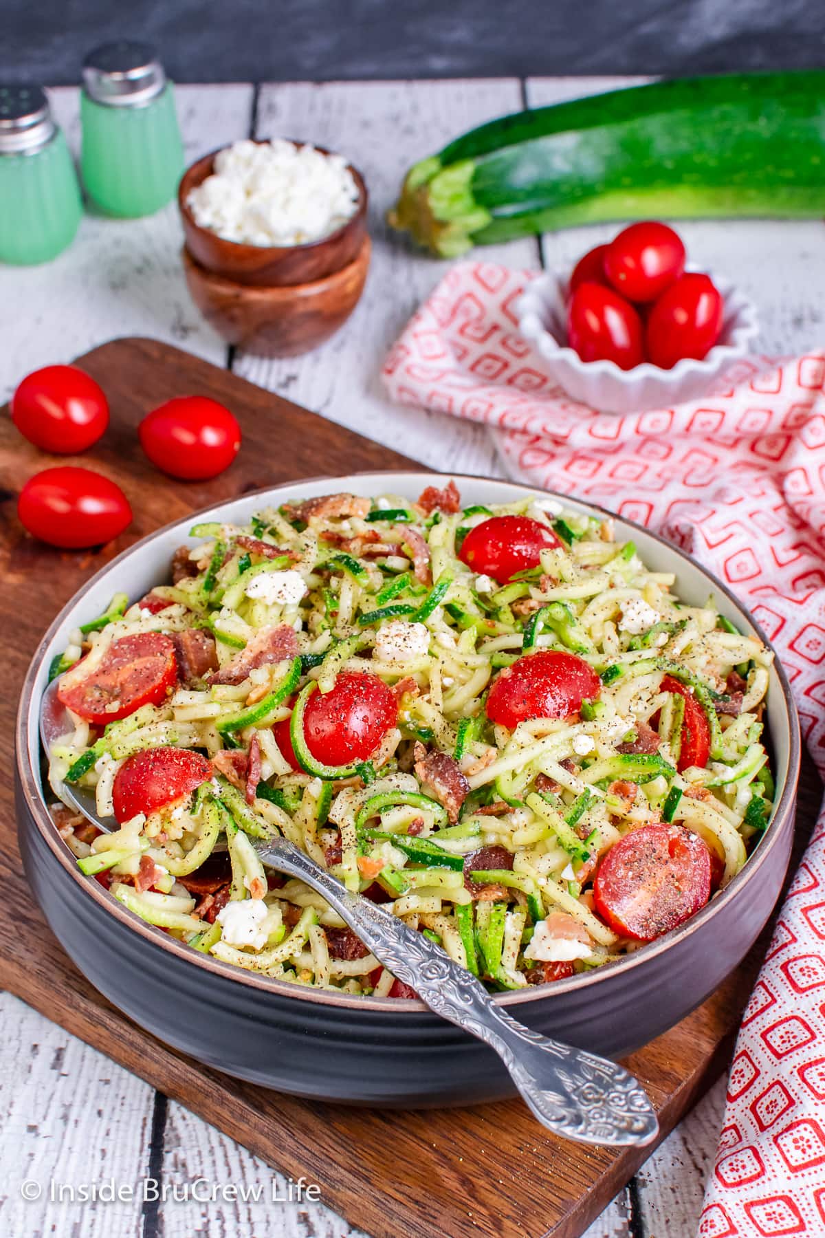 A bowl of zucchini noodles with tomatoes, feta, and bacon.