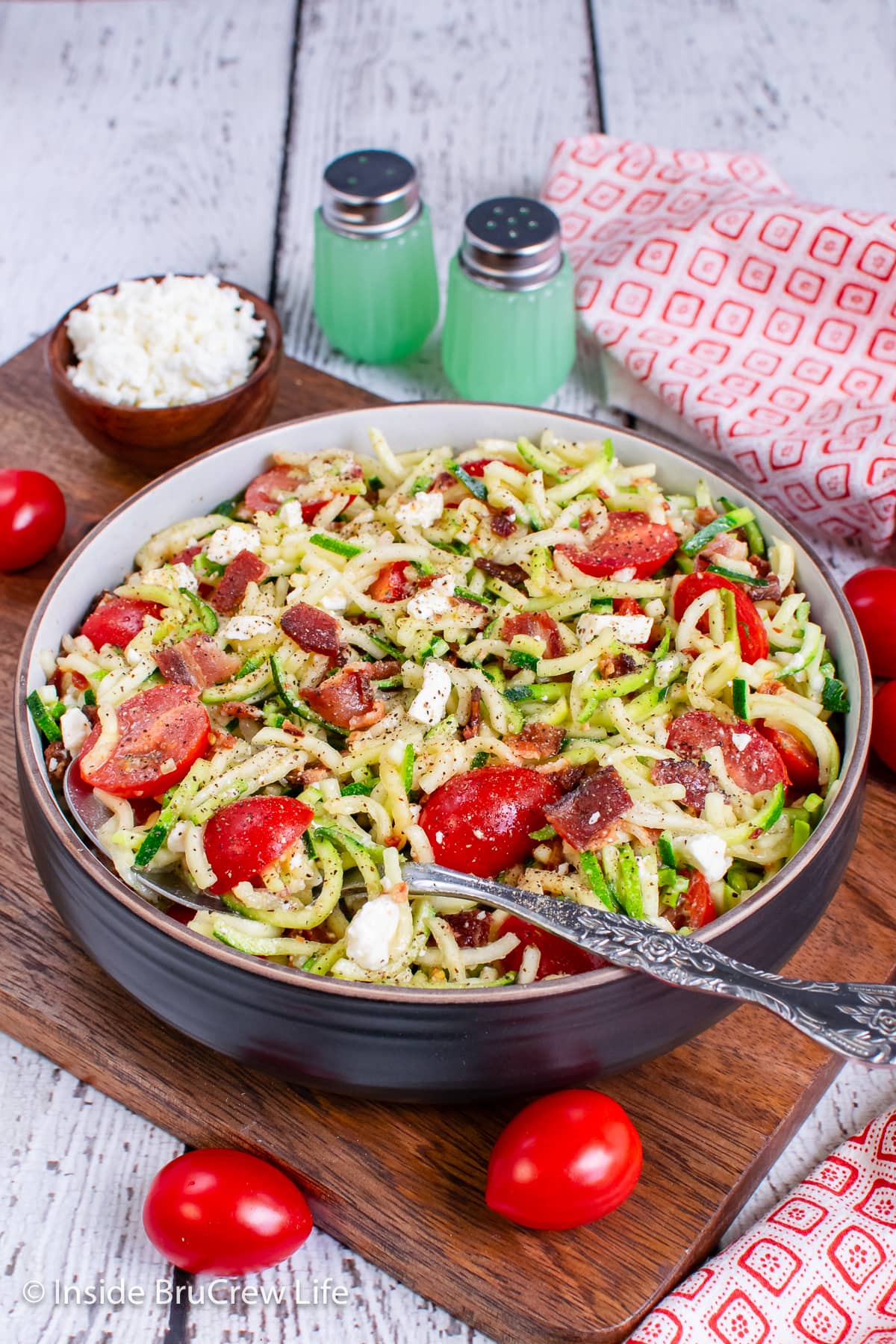 A bowl of zucchini noodles with tomatoes, feta, and bacon.