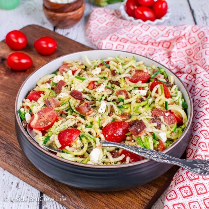 A black bowl filled with zucchini noodles and tomatoes.