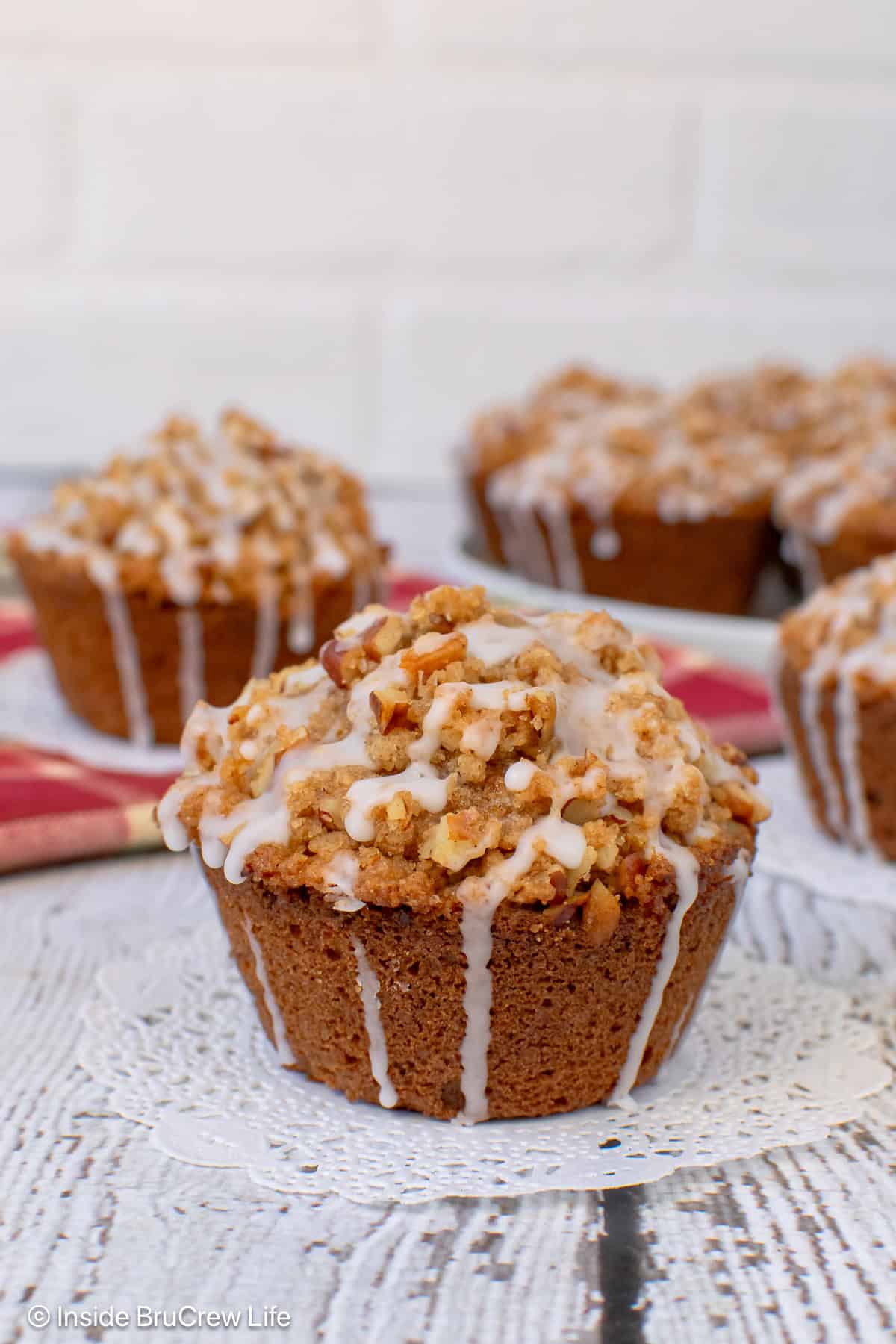 An apple pecan muffin with streusel on a white board with more muffins behind it.