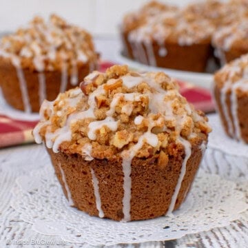 An apple pecan muffin with streusel on a white board with more muffins behind it.