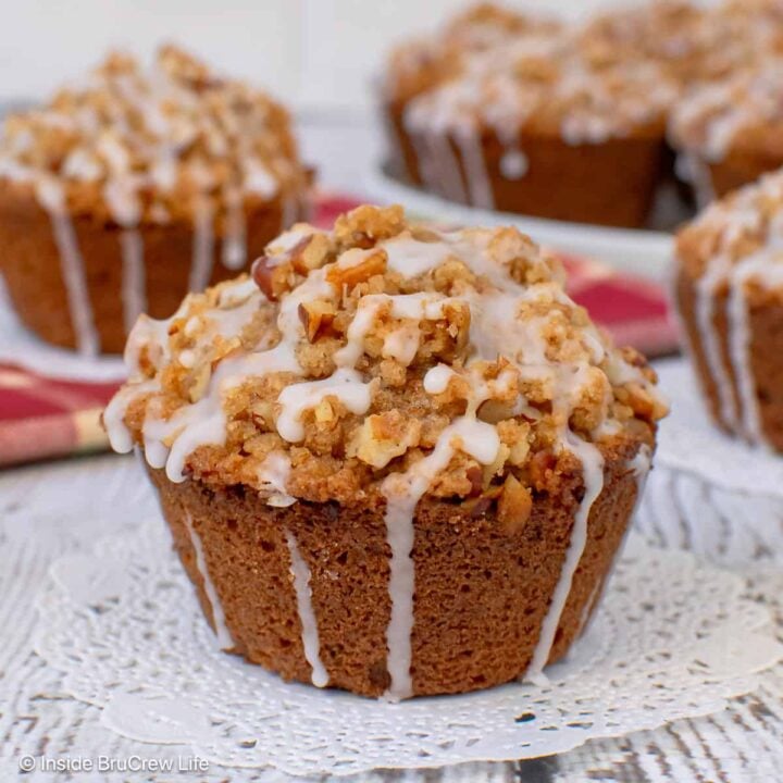 An apple pecan muffin with streusel on a white board with more muffins behind it.