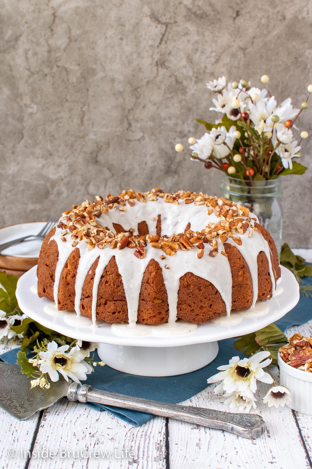 A glazed bundt cake on a white cake stand.