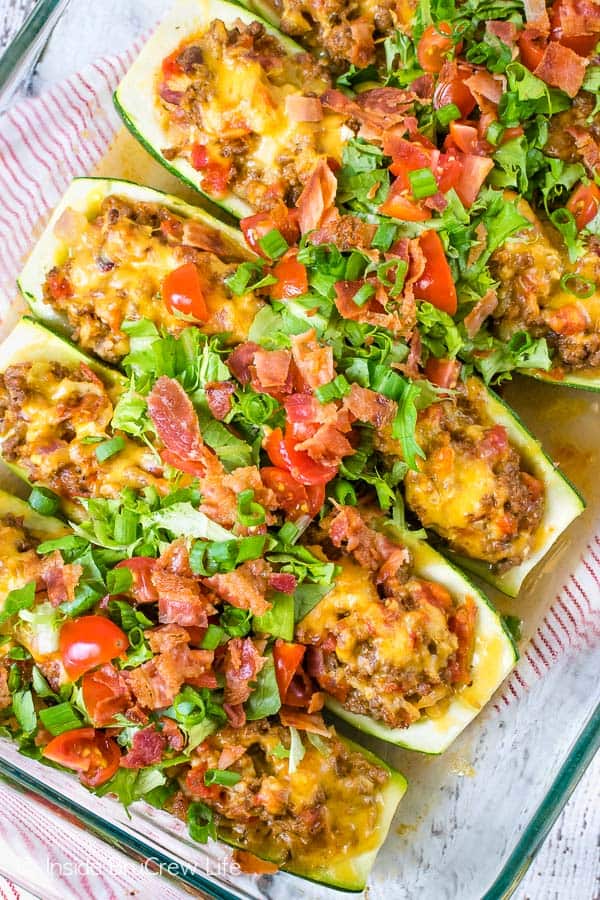 Overhead picture of cheeseburger stuffed zucchini topped with bacon, tomatoes, and lettuce.