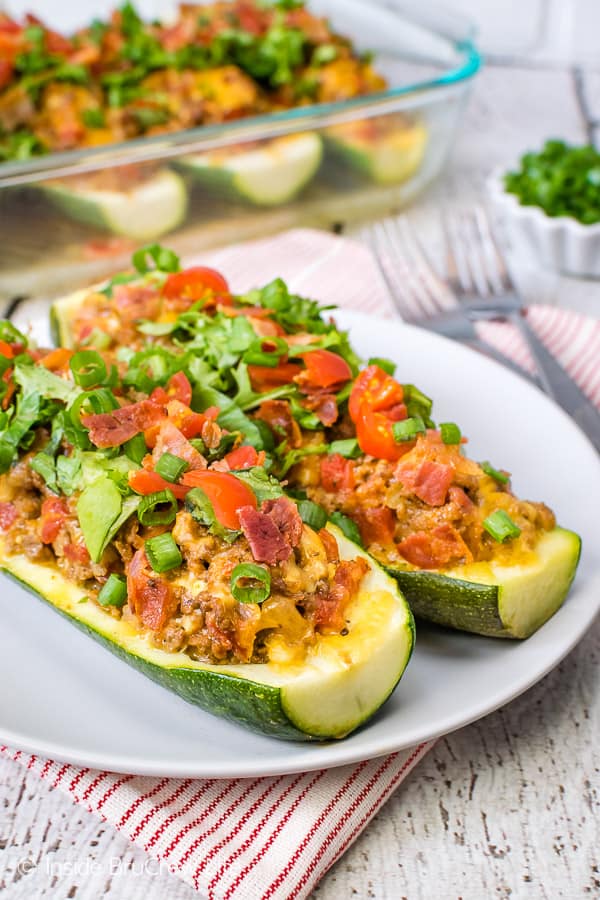 A white plate with two halves of bacon cheeseburger stuffed zucchini on it.