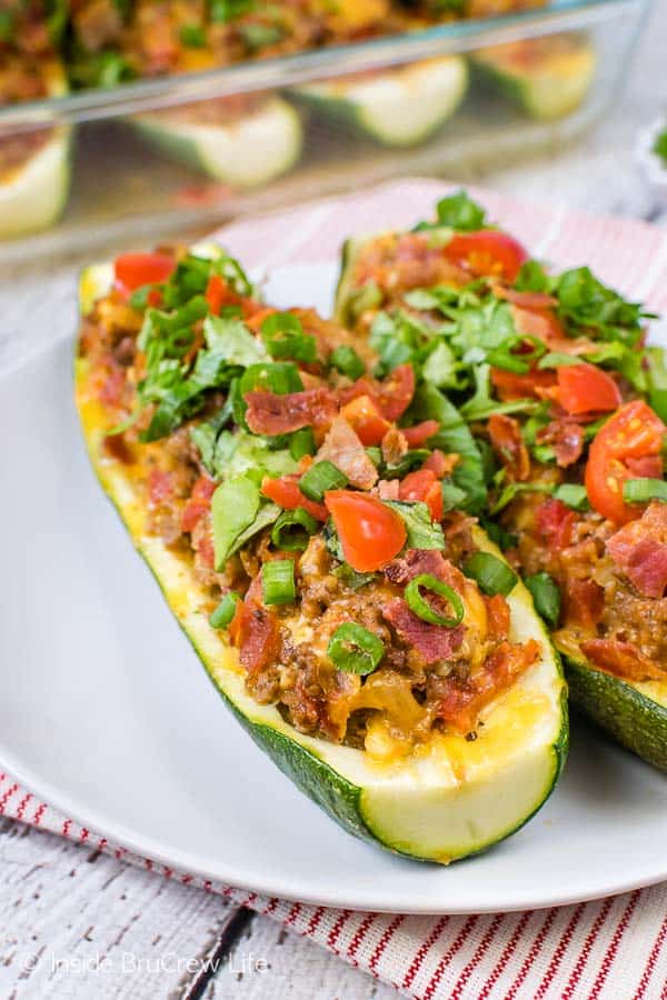 A white plate with two bacon cheeseburger zucchini boats on it.