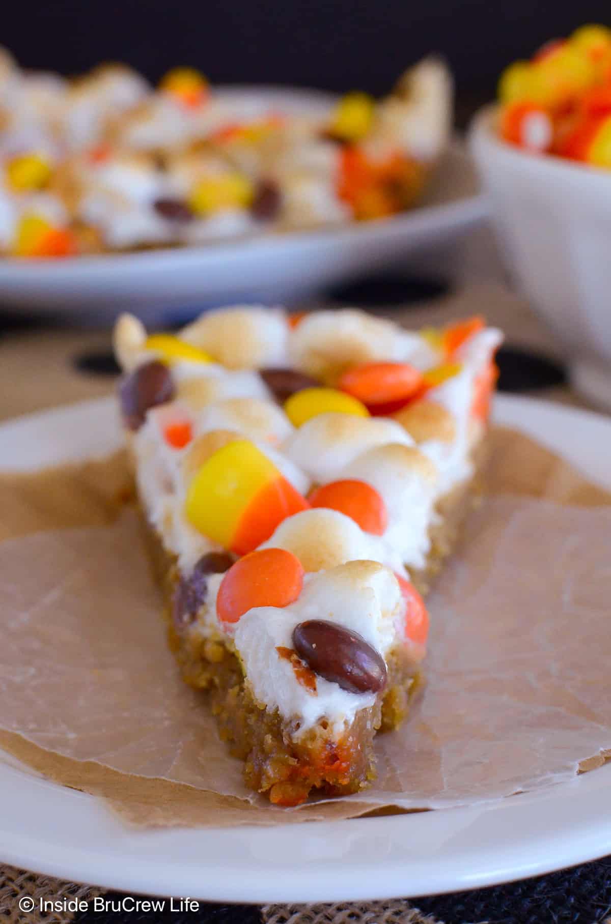 A slice of peanut butter candy corn cookie pizza on a white plate.