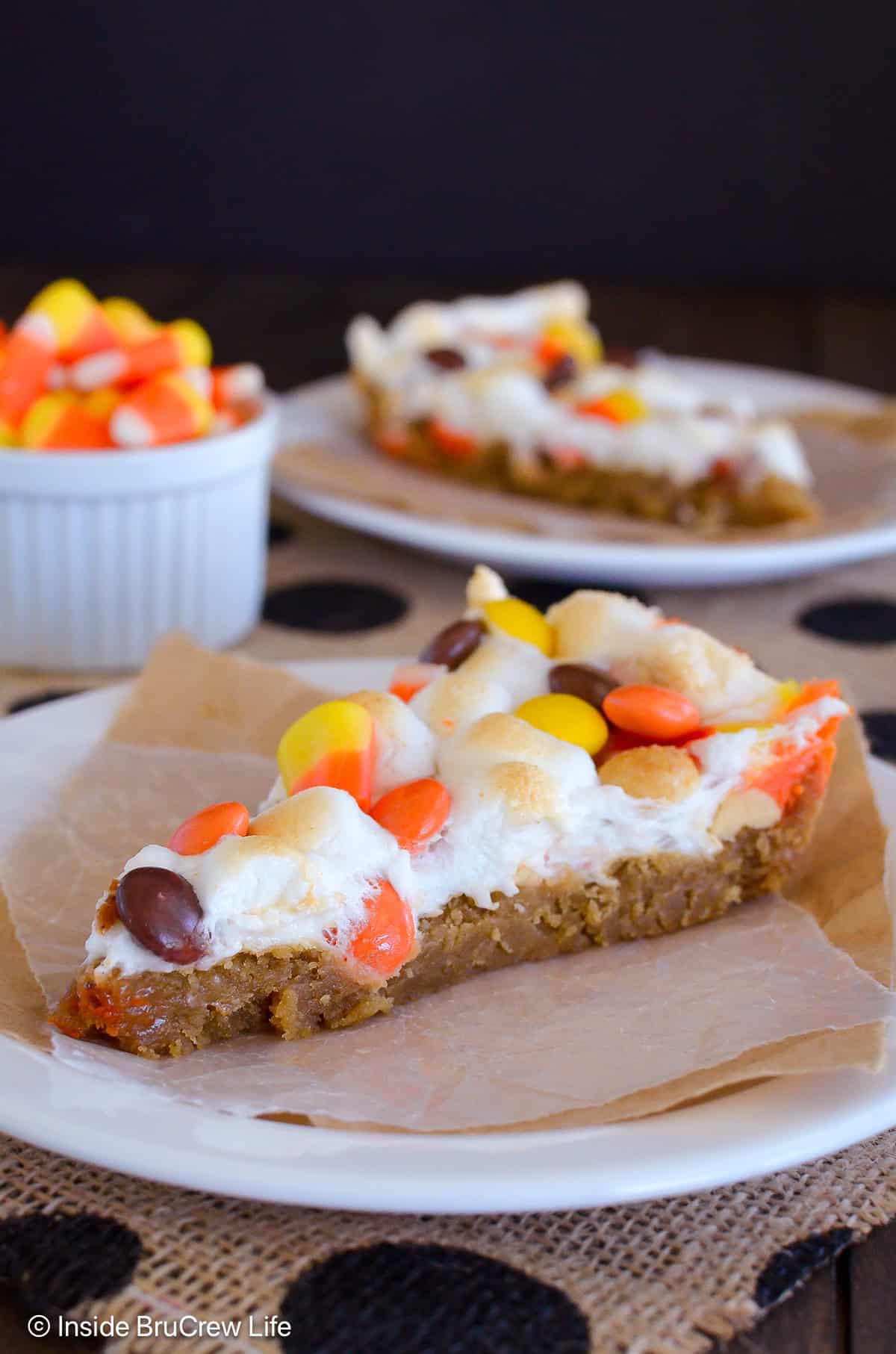Two slices of peanut butter candy corn cookie pizza on plates.