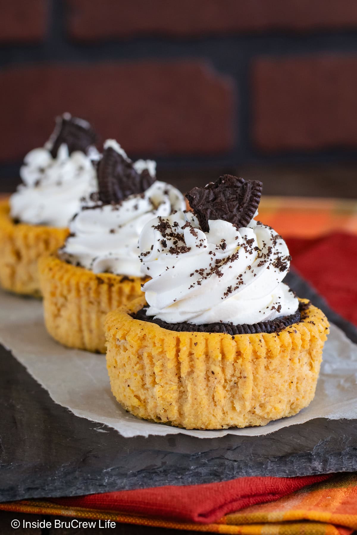 Mini pumpkin Oreo cheesecakes with whipped cream on a black tray.