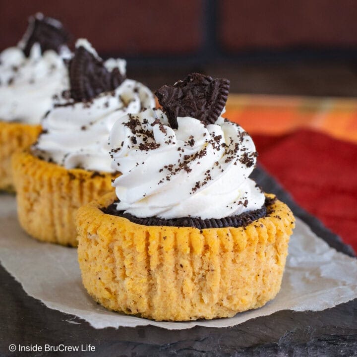 Mini pumpkin Oreo cheesecakes with whipped cream on a black tray.