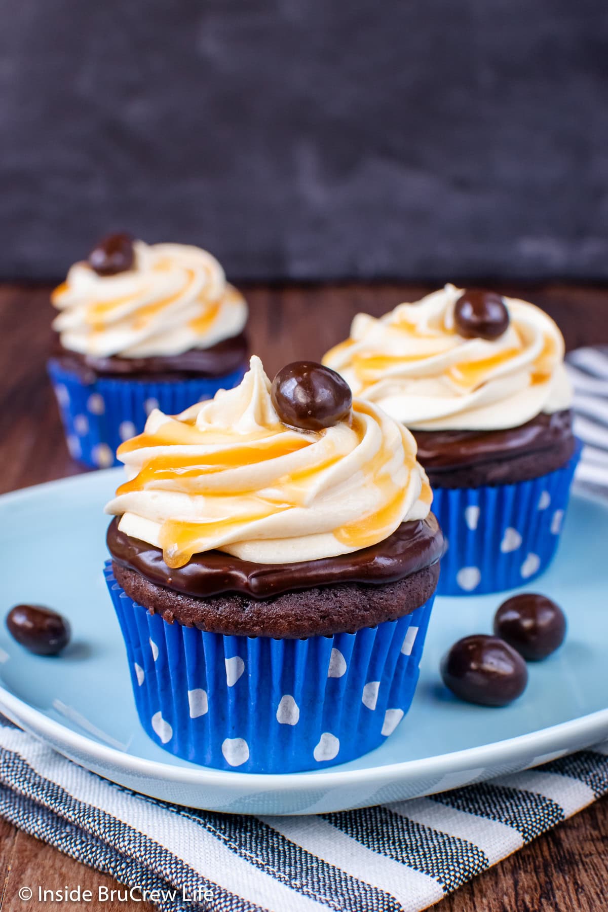 Three chocolate cupcakes with caramel frosting on a plate.
