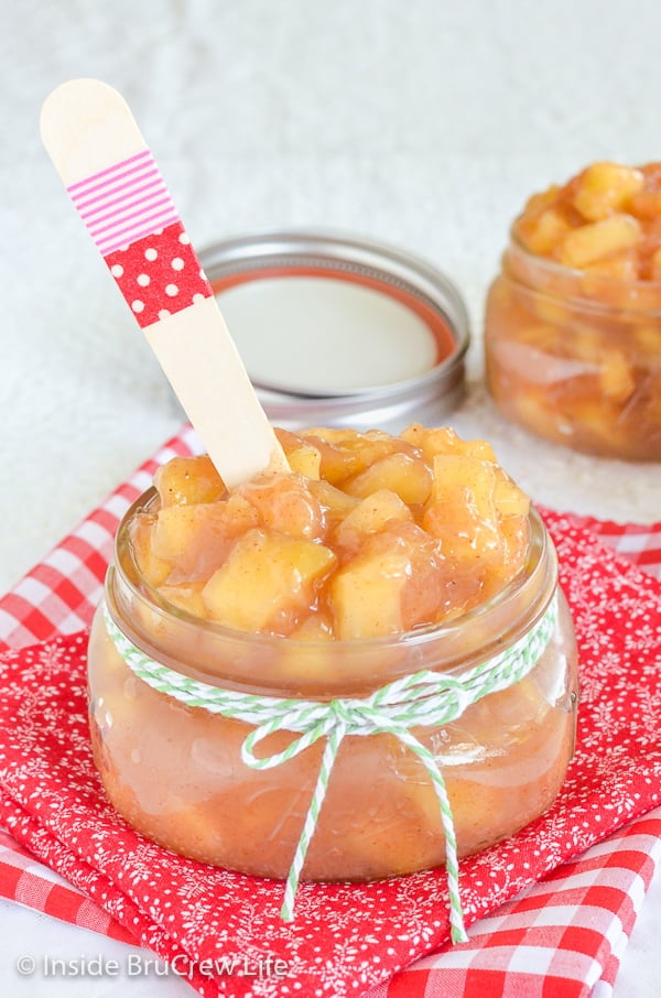 A red towel with a clear jar with twine on it filled with apple pie filling and a wooden spoon