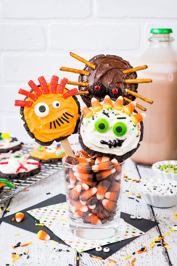 Three monster sugar cookies on sticks placed in a jar of candy corn.