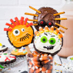 Three chocolate monster cookies on a stick decorated with candies and frosting.