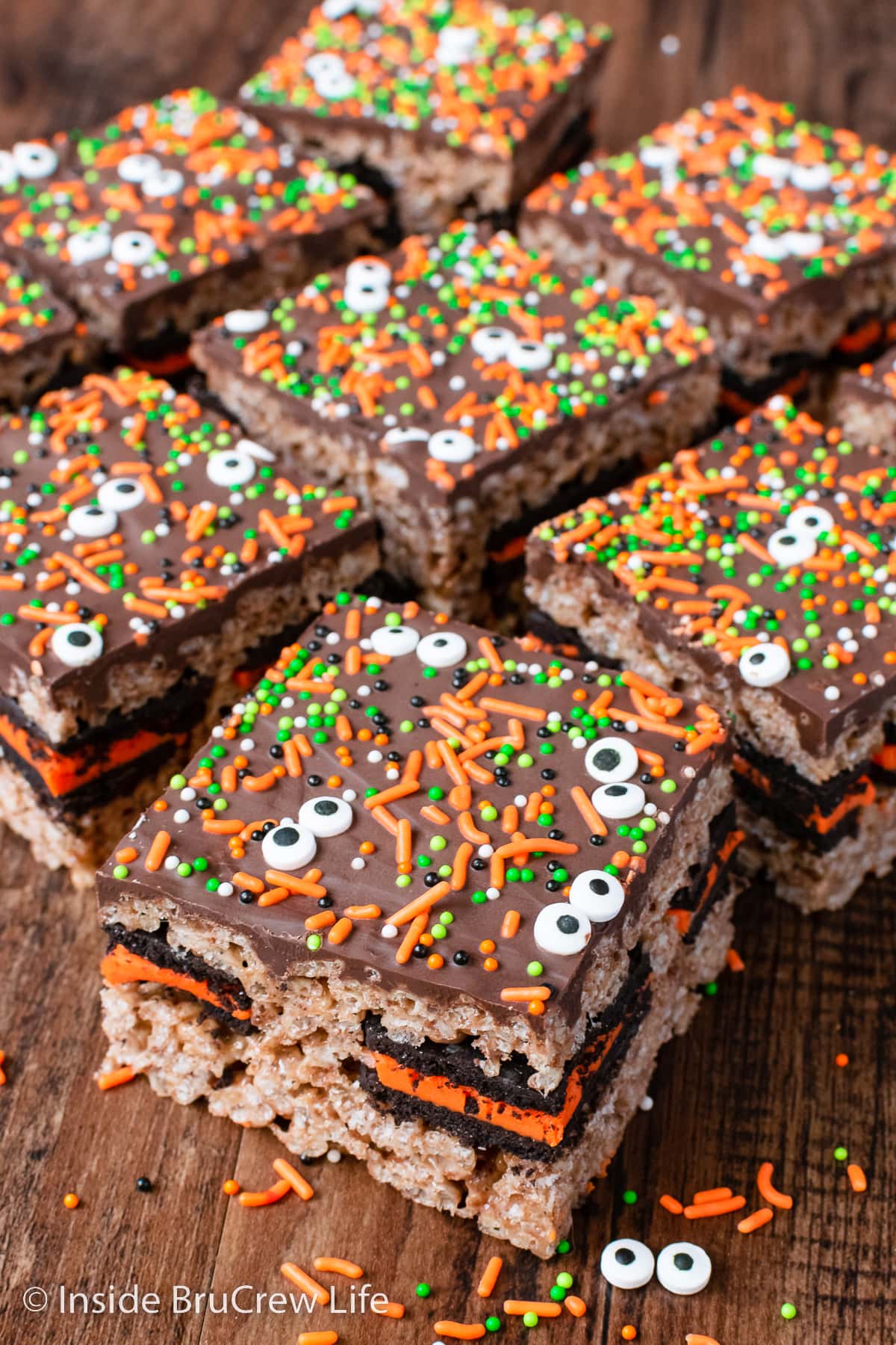 Rice krispie treats topped with chocolate and sprinkles on a brown board.
