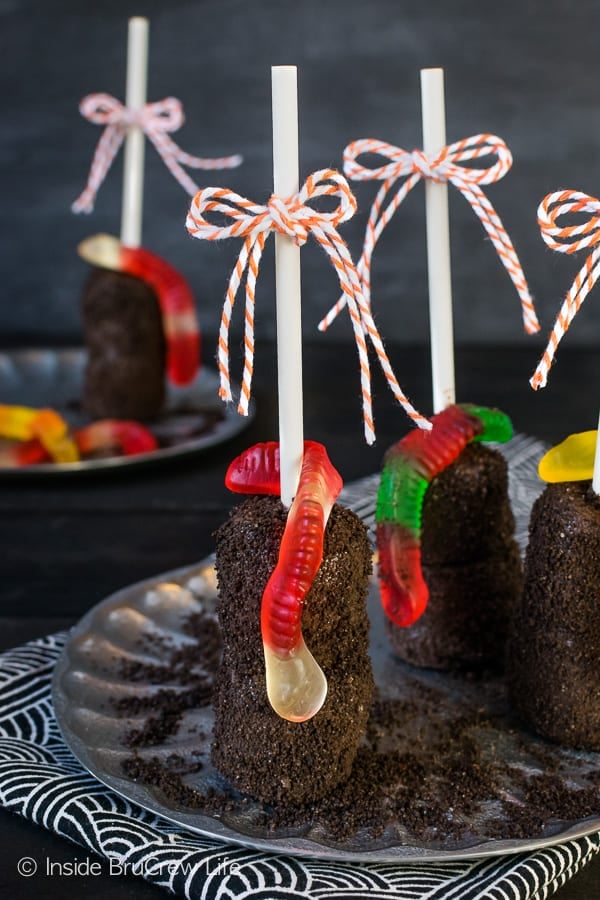 Dirt Marshmallow Pops - a gummy worm and cookie "dirt" makes these chocolate covered marshmallows a fun party treat. Share this no bake recipe at Halloween parties! #halloween #dirtdessert #marshmallowpops #chocolatecoveredmarshmallows #gummyworms #halloween #nobakedessert #chocolate #marshmallows