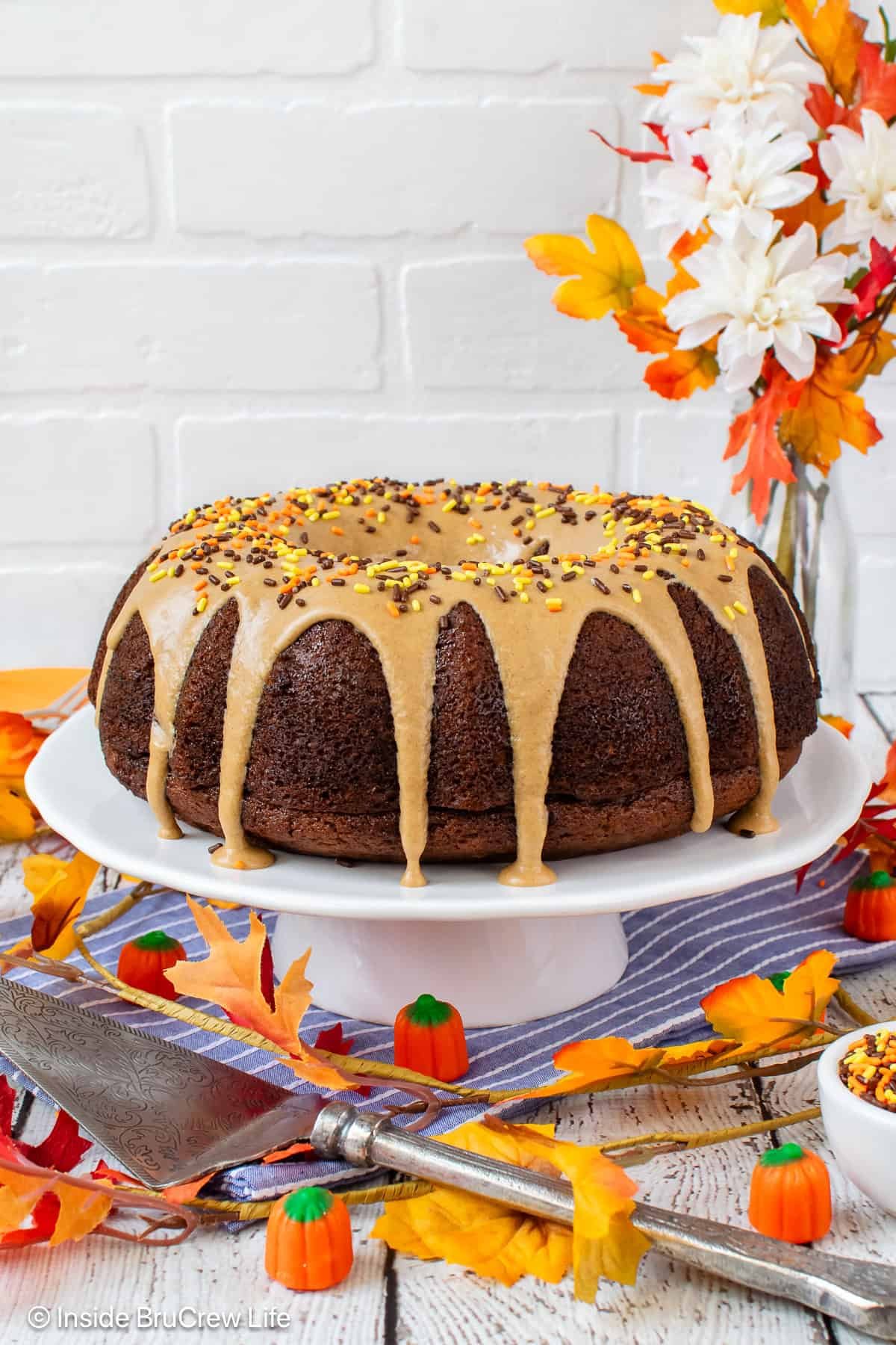 A glazed pumpkin bundt cake on a white cake stand.