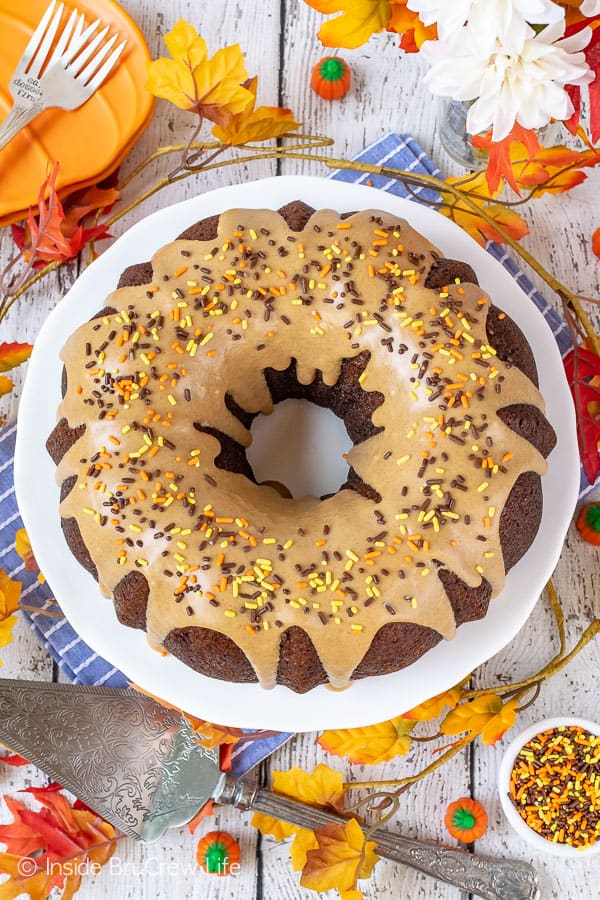 Overhead picture of a pumpkin bundt cake on a white cake plate topped with maple glaze and sprinkles.