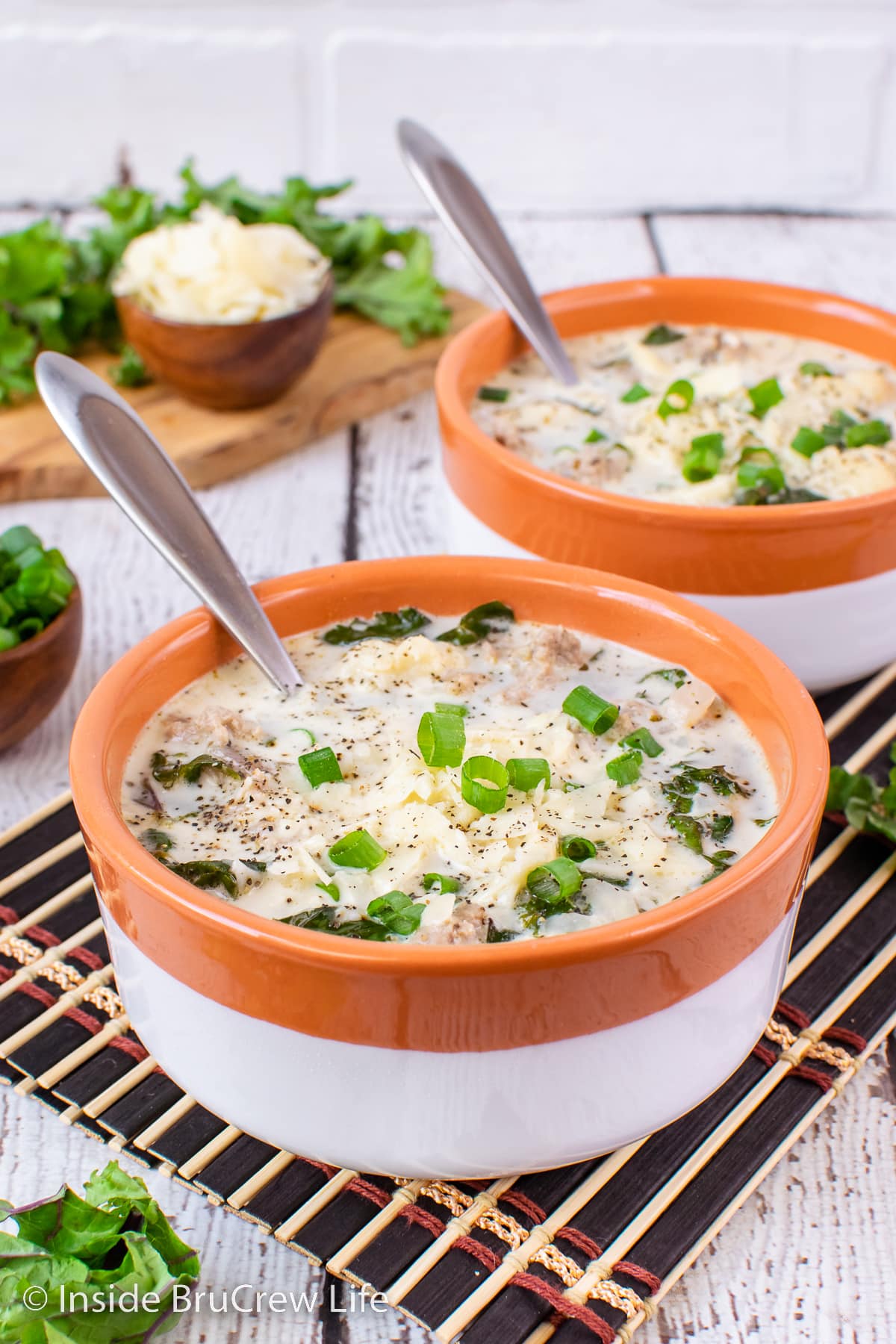 Two bowls filled with creamy kale soup and topped with cheese and onions.