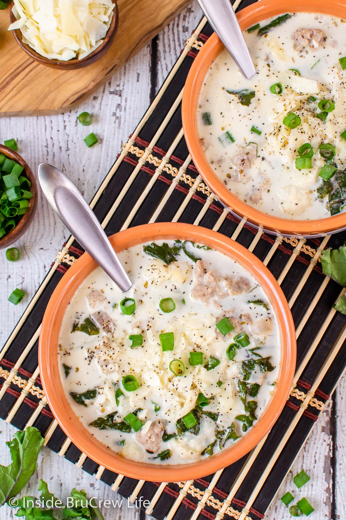 A bowl of creamy sausage soup topped with cheese and onions.