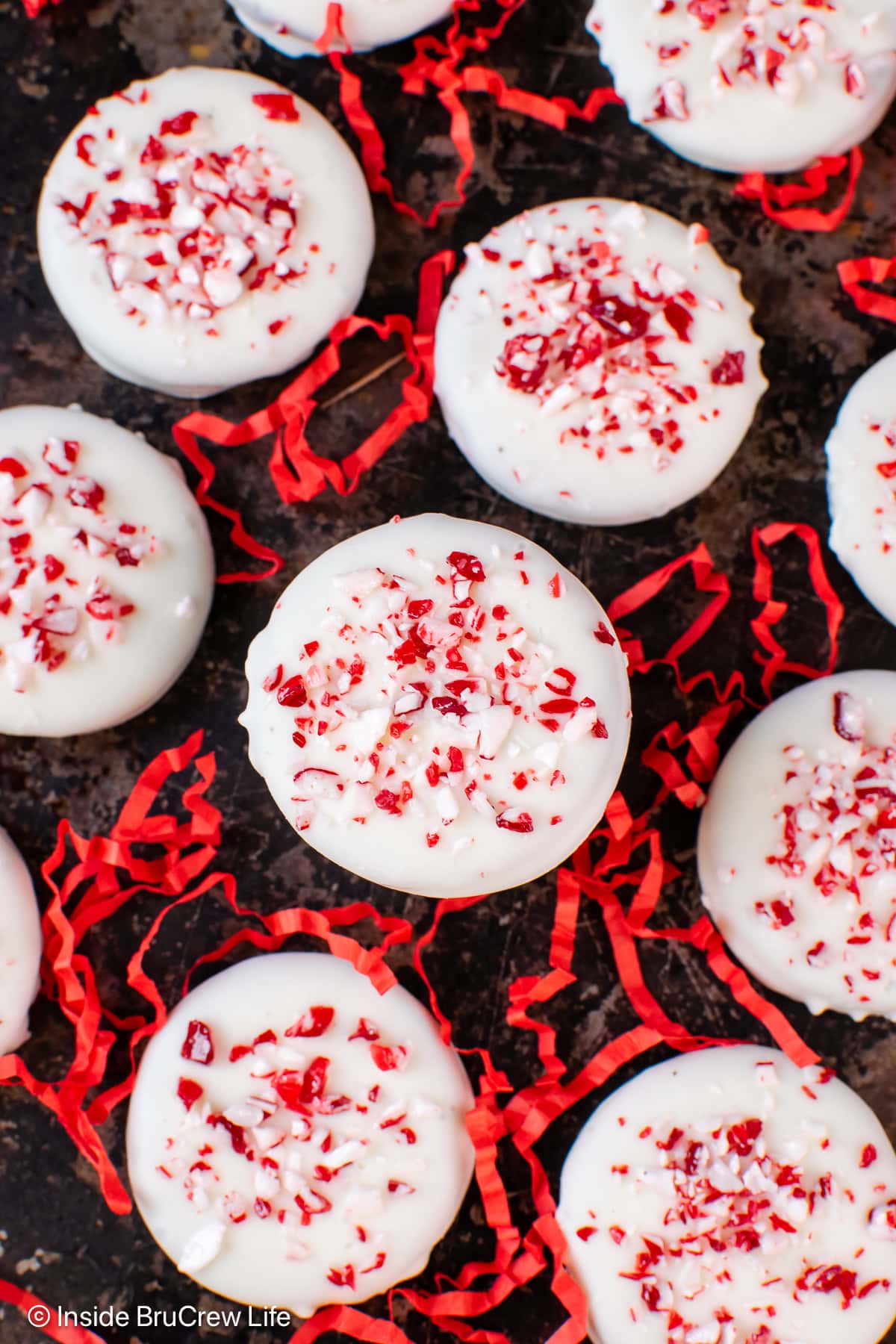 A black tray with red ribbons and white chocolate dipped Oreos on it.