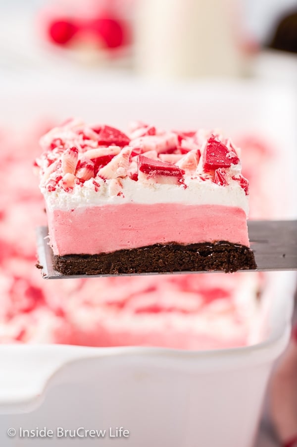 A spatula lifting up a square of Peppermint Oreo Cheesecake out of a white pan.