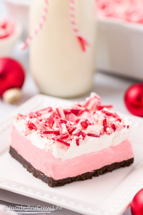 A white plate with a slice of no bake peppermint cheesecake topped with peppermint crunch chips on top.