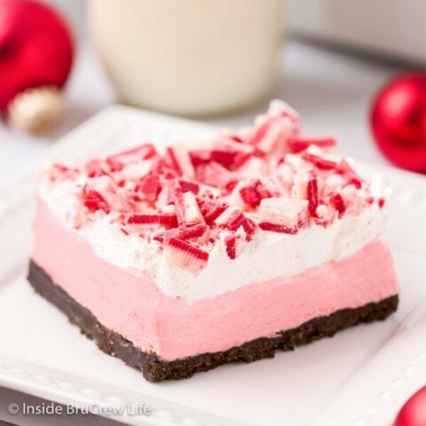 A white plate with a square of peppermint cheesecake topped with crunch chips on it.