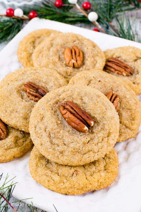 A white plate with a stack of maple cookies topped with pecans on it.
