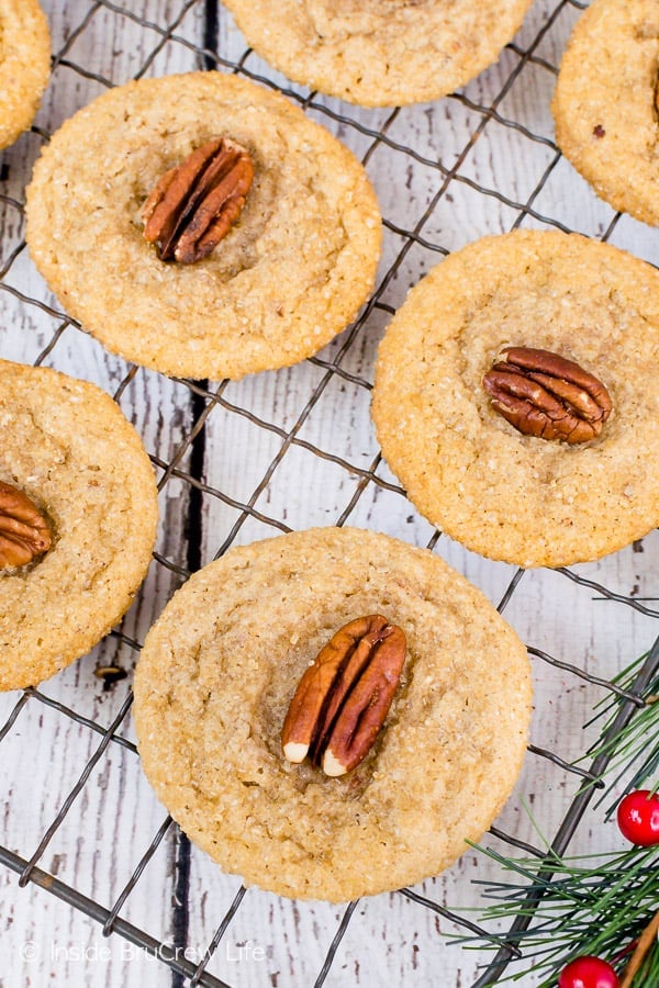 A metal wire rack with maple cookies topped with pecans on top of it.
