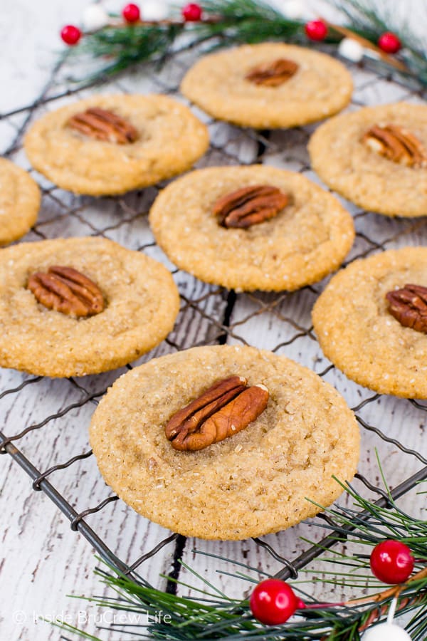 A wire rack with a layer of spiced maple cookies topped with pecans on it.