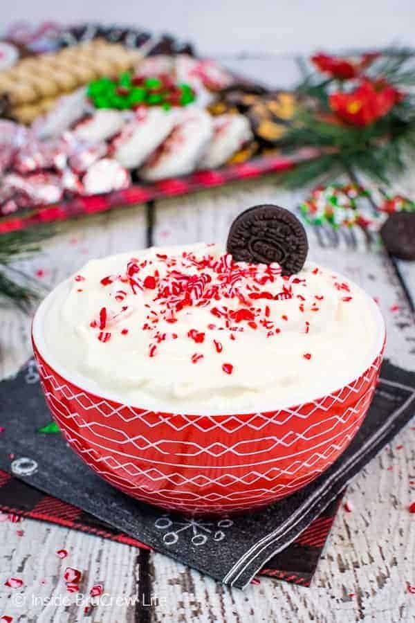 A red bowl of White Chocolate Peppermint Cheesecake Dip with cookies in the background.