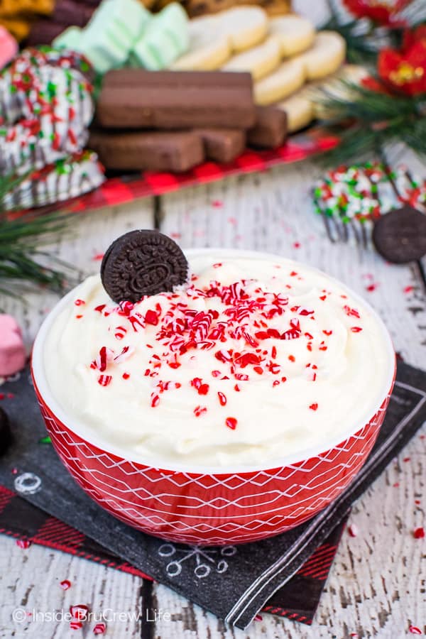 A red bowl of White Chocolate Peppermint Cheesecake Dip with cookies in the background.