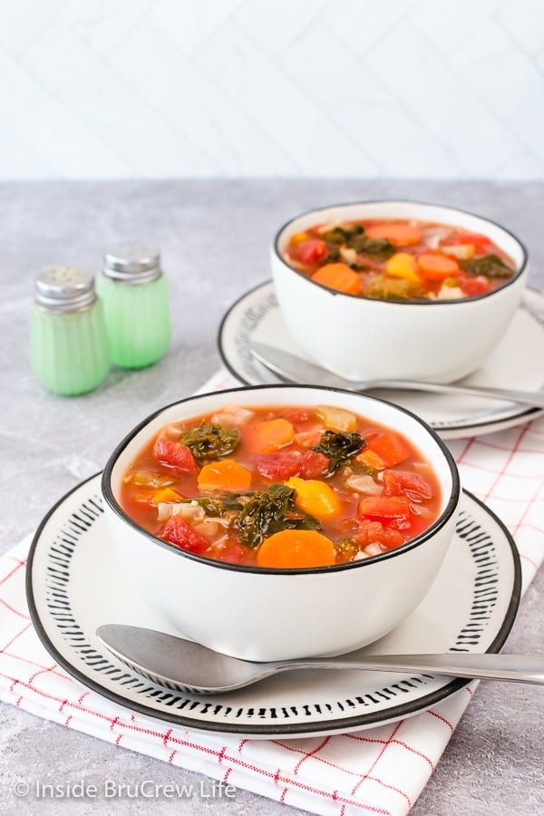 Two white bowls on white plates filled with healthy vegetable soup.
