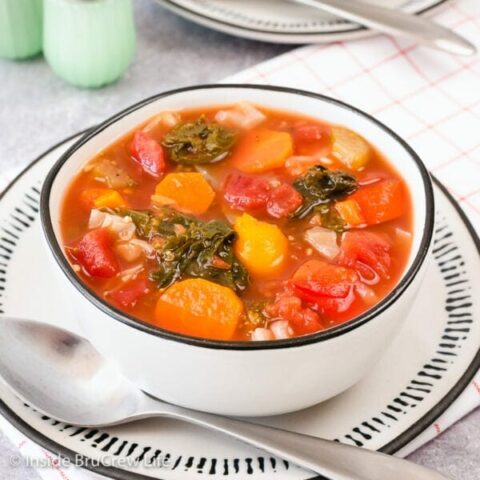 A white bowl on a white plate filled with vegetable soup.