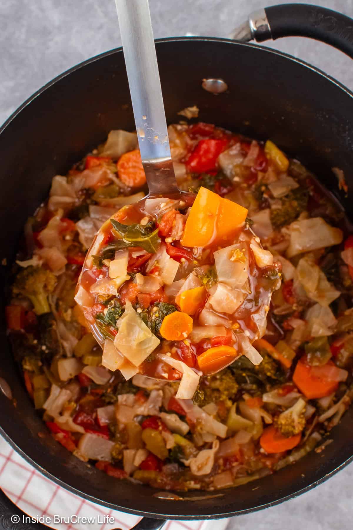 A black pot of veggie soup with a ladle lifting out a scoop.