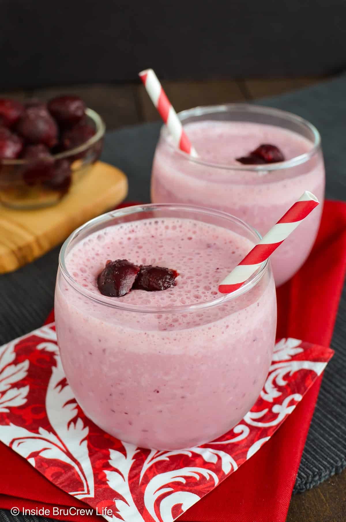 Two clear glasses filled with a cherry smoothie.