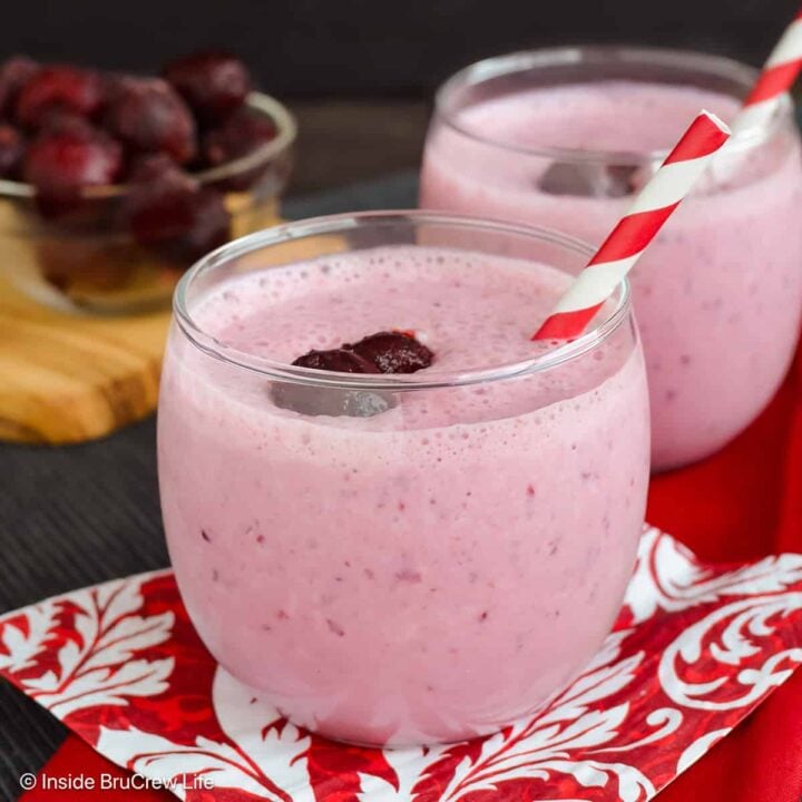 Two glasses filled with a cherry banana smoothie and a paper straw.