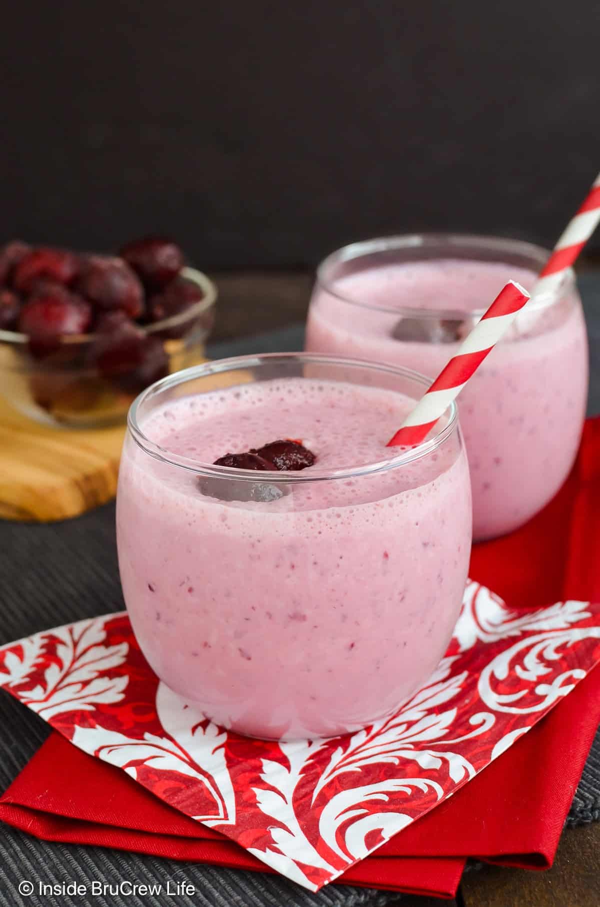Two glasses filled with a cherry banana smoothie and a paper straw.
