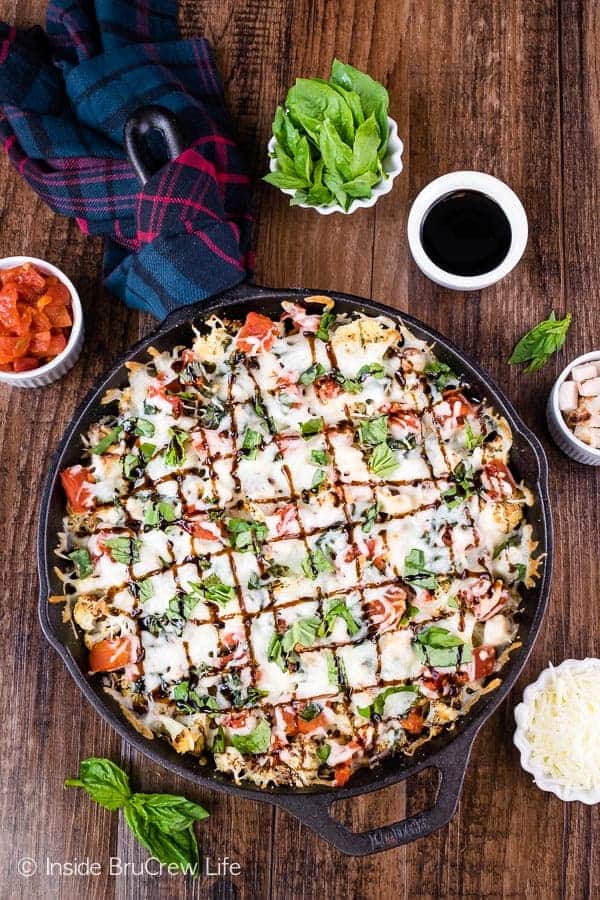 An overhead picture of a cast iron skillet with cauliflower nachos topped with cheese, chicken, and basil in it.