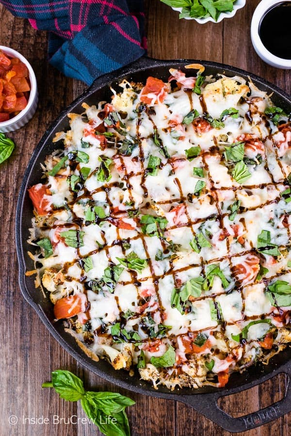 Overhead picture of a black cast iron pan with cauliflower nachos topped with cheese, chicken, and tomatoes in it.