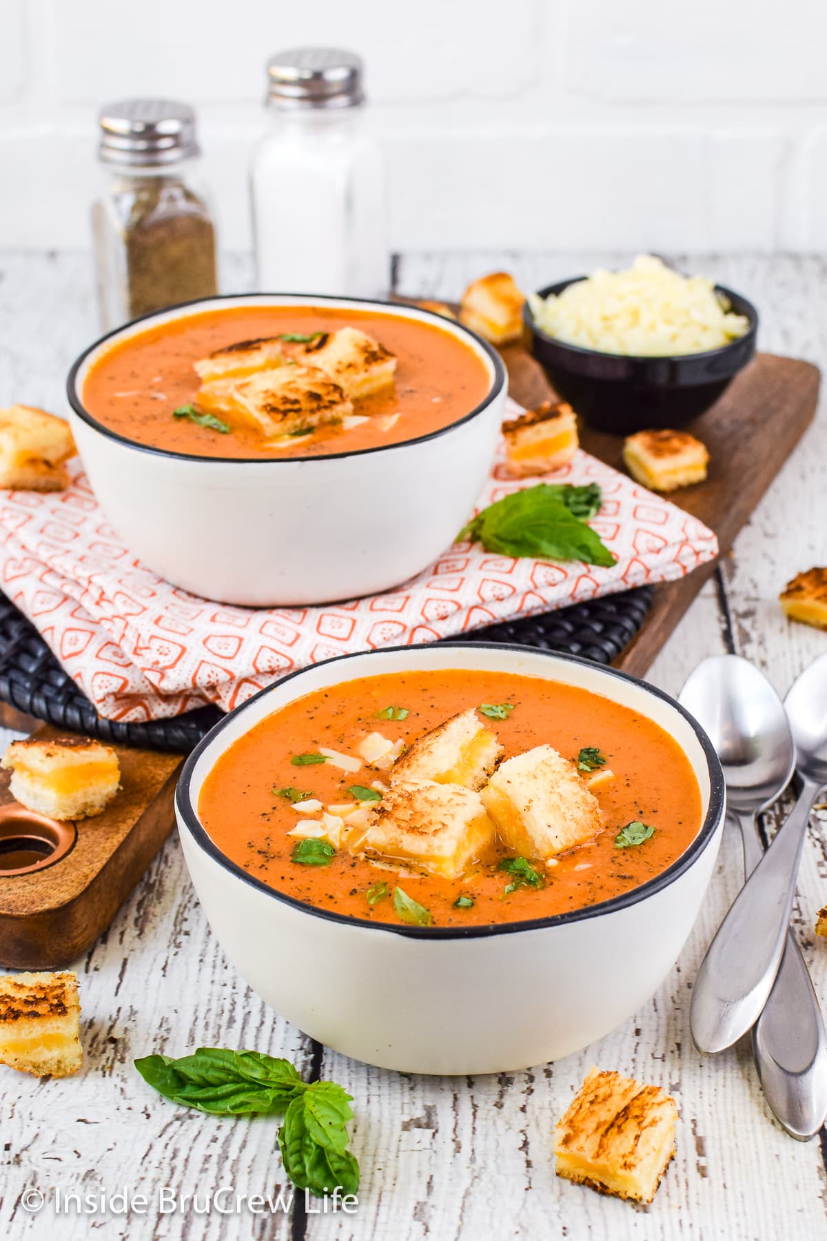 Two bowls of tomato soup with grilled cheese cubes floating in them.