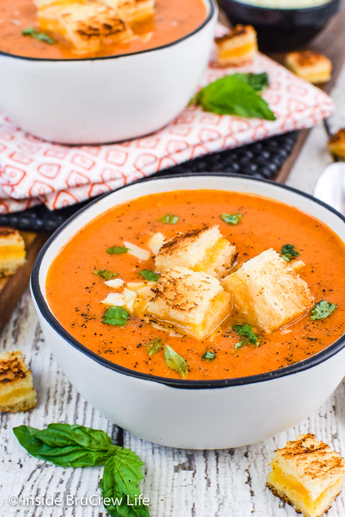 A white bowl filled with tomato soup and topped with grilled cheese squares.