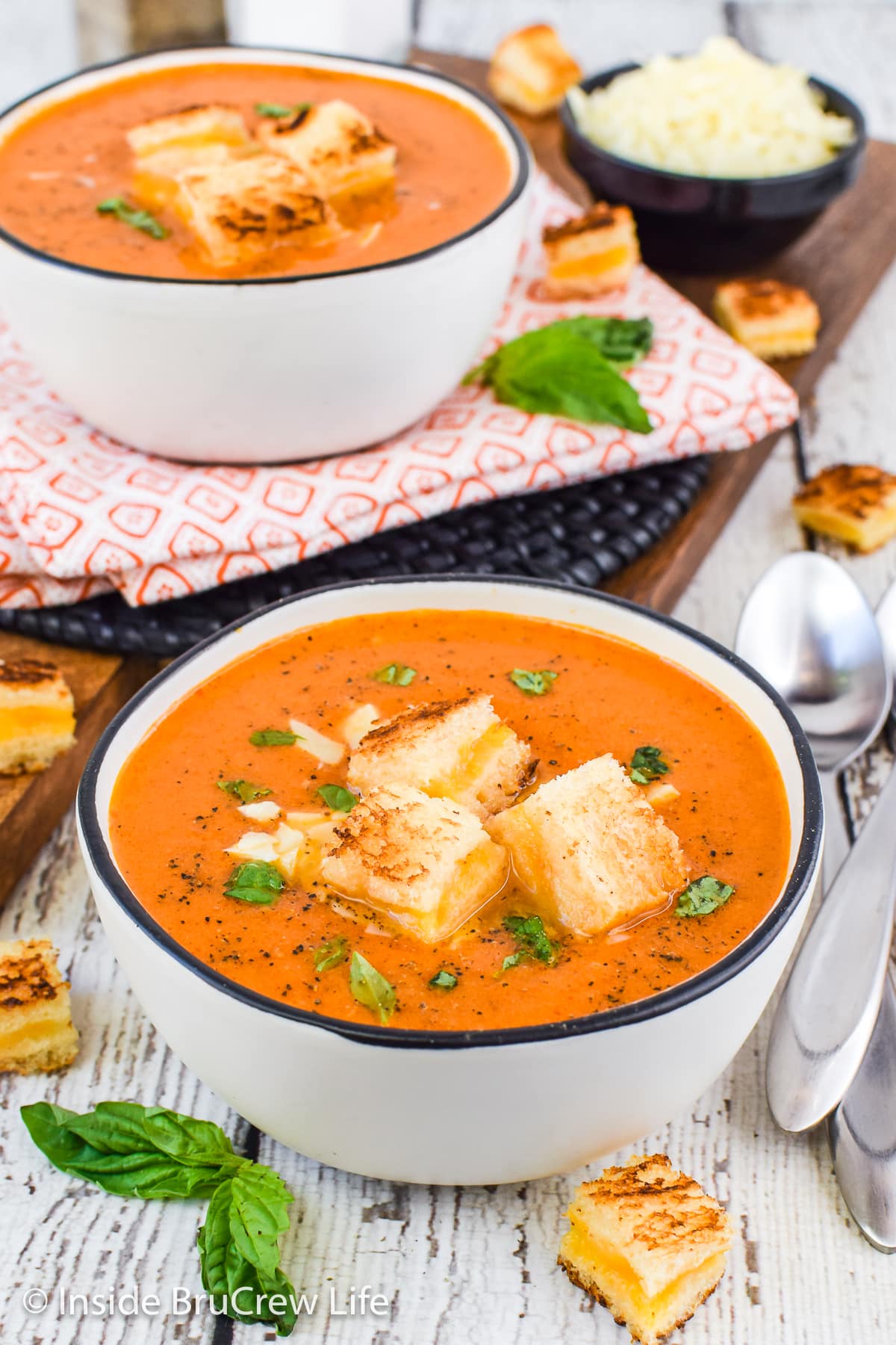 Two bowls of tomato soup with grilled cheese cubes floating in them.