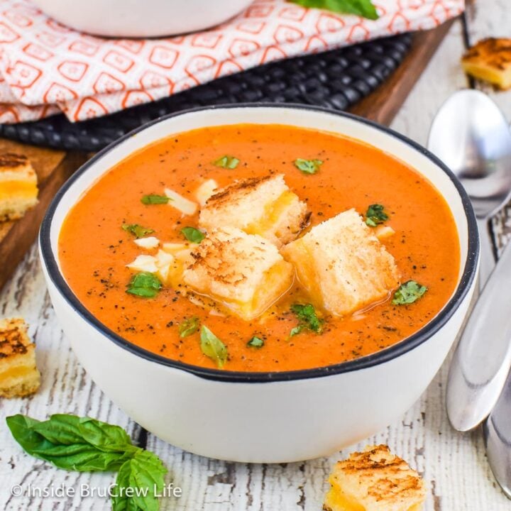 A bowl of creamy tomato soup with grilled cheese squares on top.