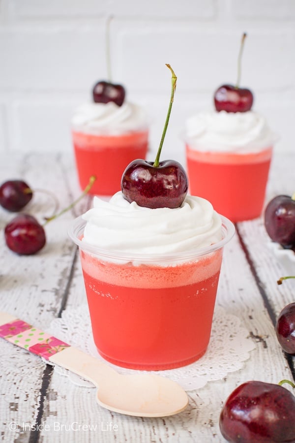 Three clear parfait cups filled with low carb cherry jello layers and topped with reddi whip and a cherry