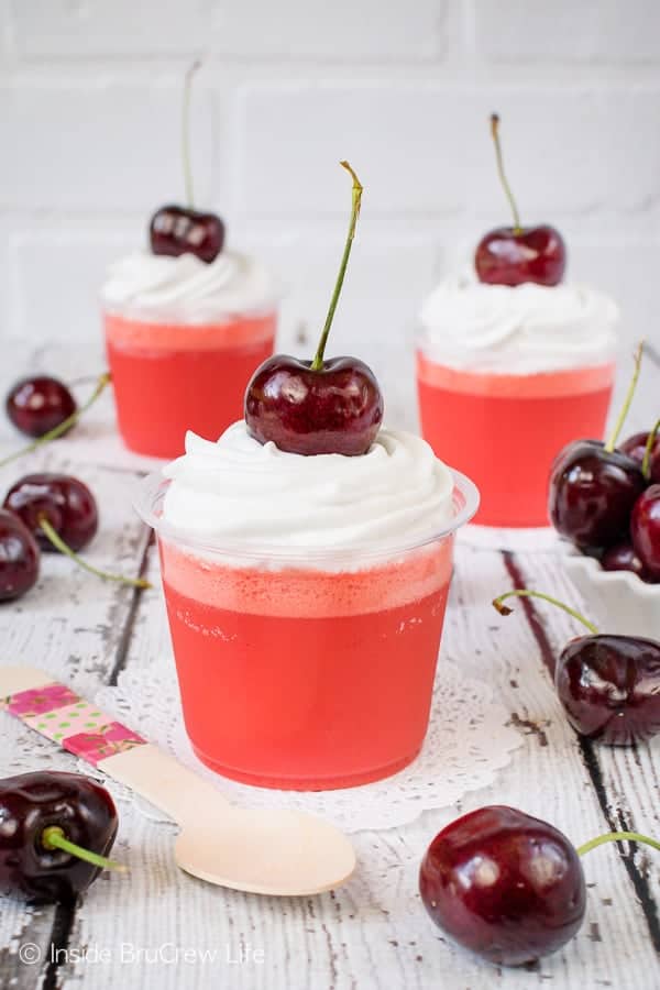 Three clear cups filled with low carb cherry jello parfaits and topped with reddi whip and a cherry
