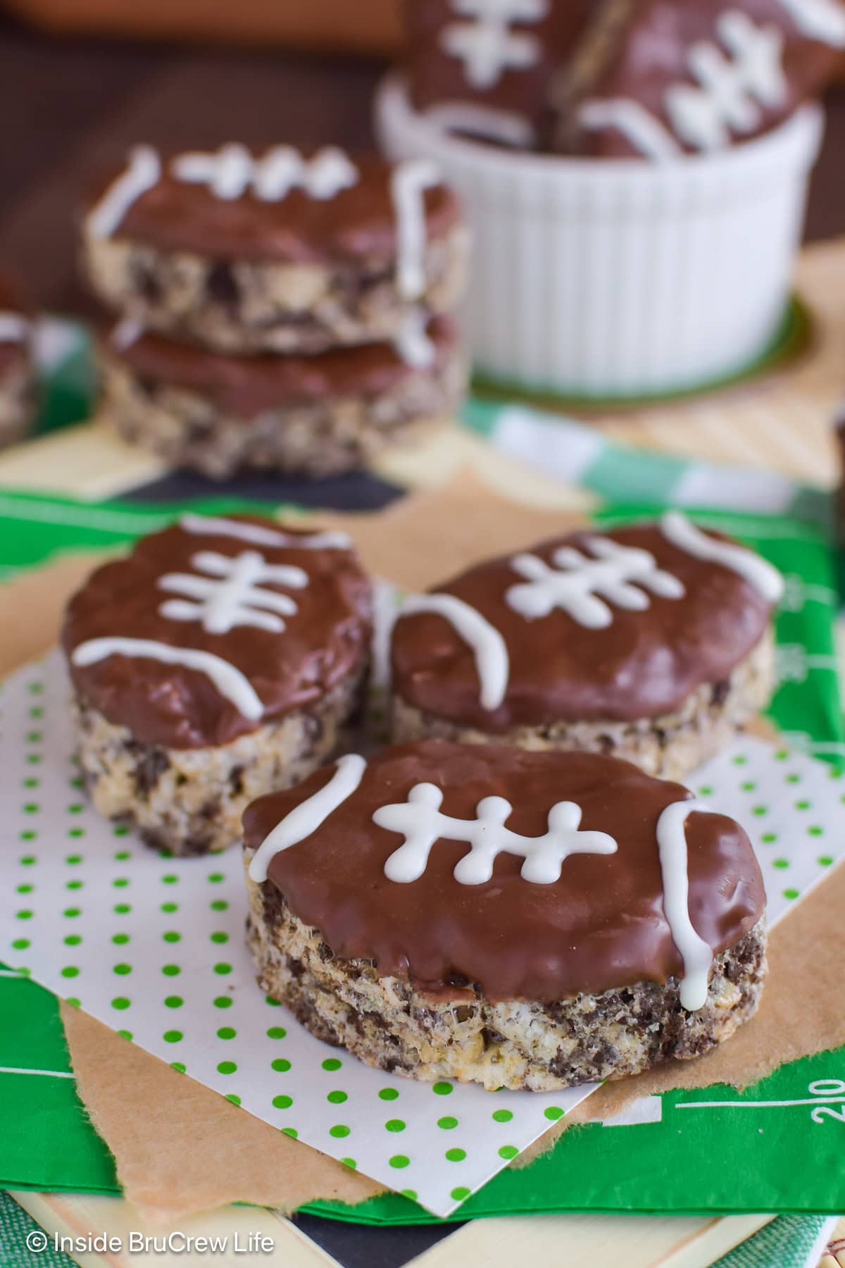 Football shaped rice krispie treats lying on green and white napkins.