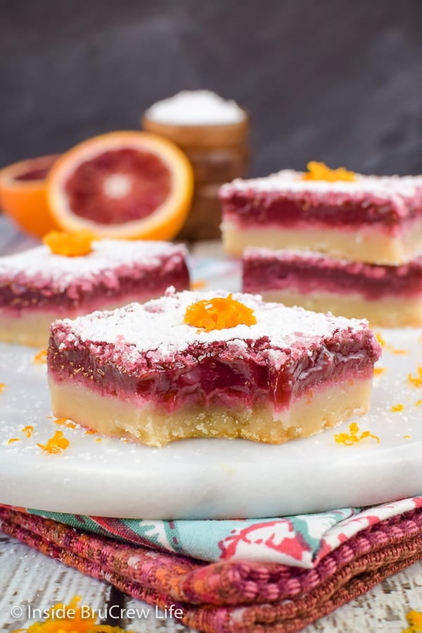 A white tray with squares of orange bars topped with powdered sugar on it.